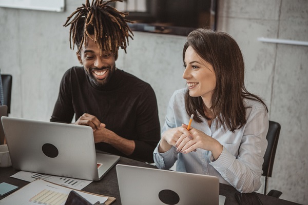 Deux collègues travaillent côte à côte devant leurs ordinateurs portables, décontractés, souriants